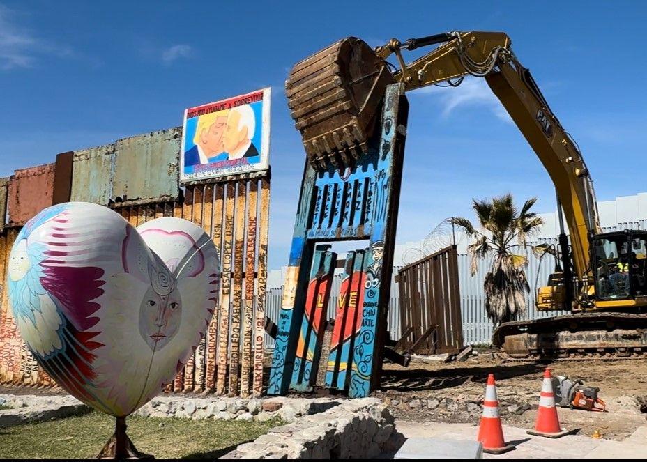 A photo of a border wall panel being taken down by an excavator.