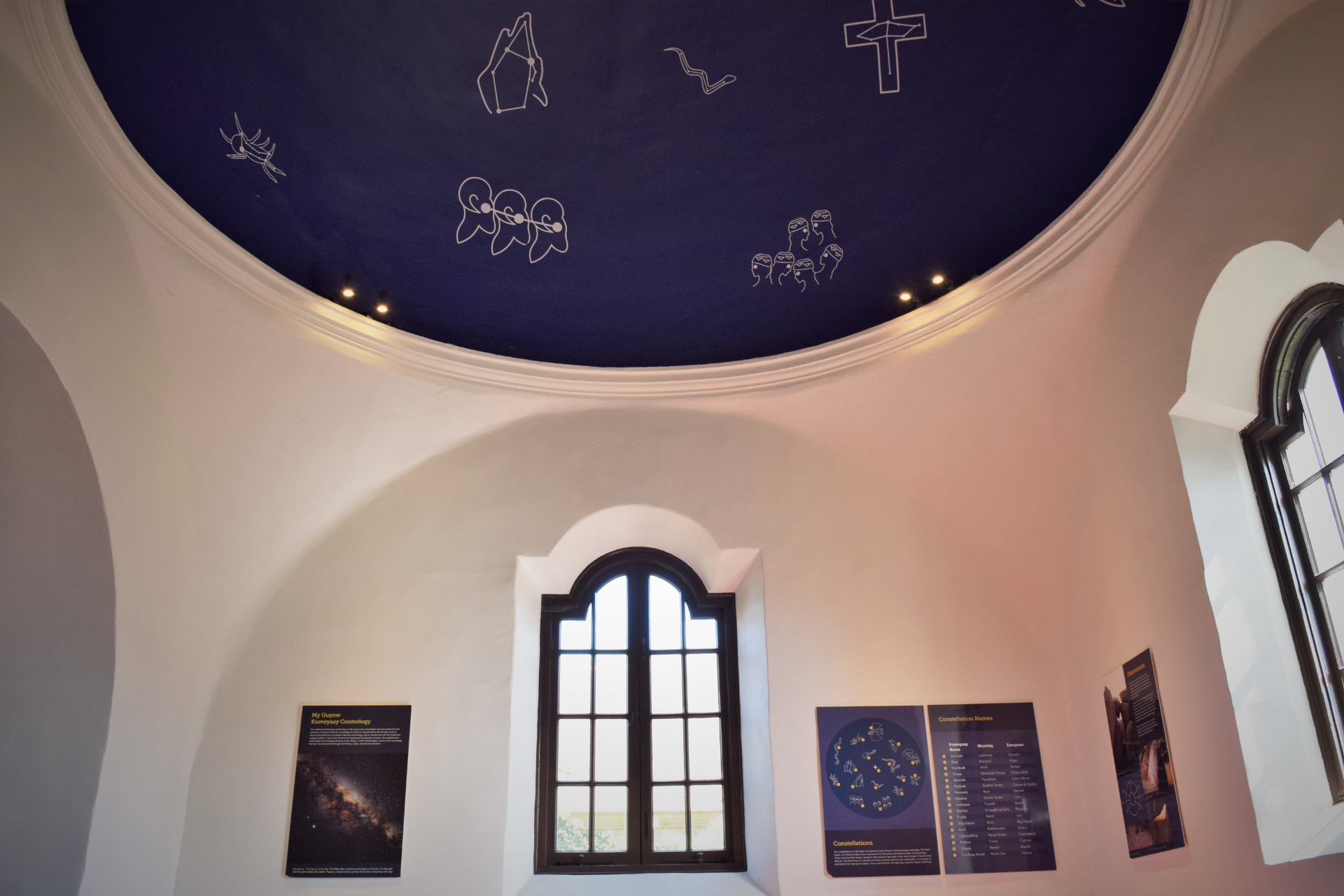 A room with constellations on the ceiling and text panels on the walls describing the stars and constellations in the Kumeyaay Cosmology Dome exhibit. 