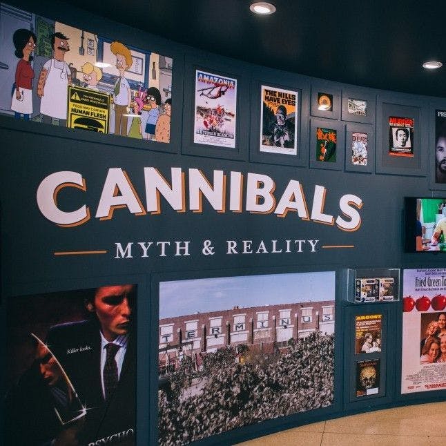 Graphic installation of various movie posters and prints hung on an exhibition wall titled 'Cannibals: Myth & Reality'