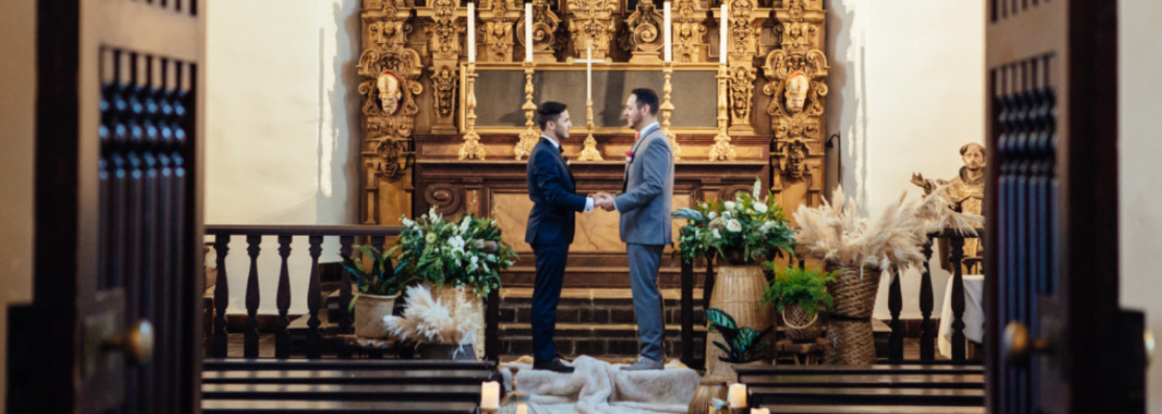 Two men facing each other and holding hands in front of the organ in the St. Francis Chapel.
