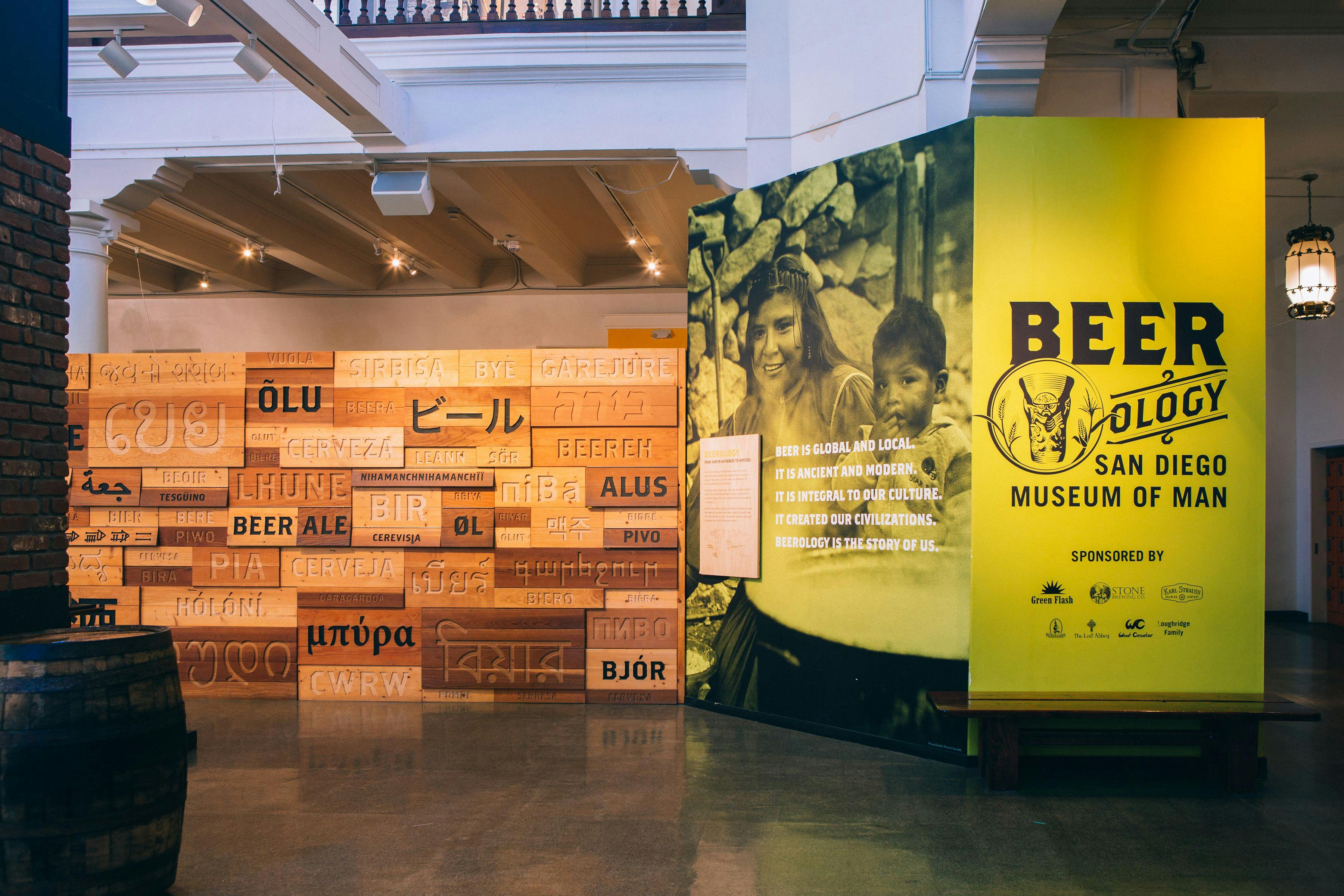 Exhibit entrance wall of "BEERology" featuring a wooden panel of the word "beer" in different languages.