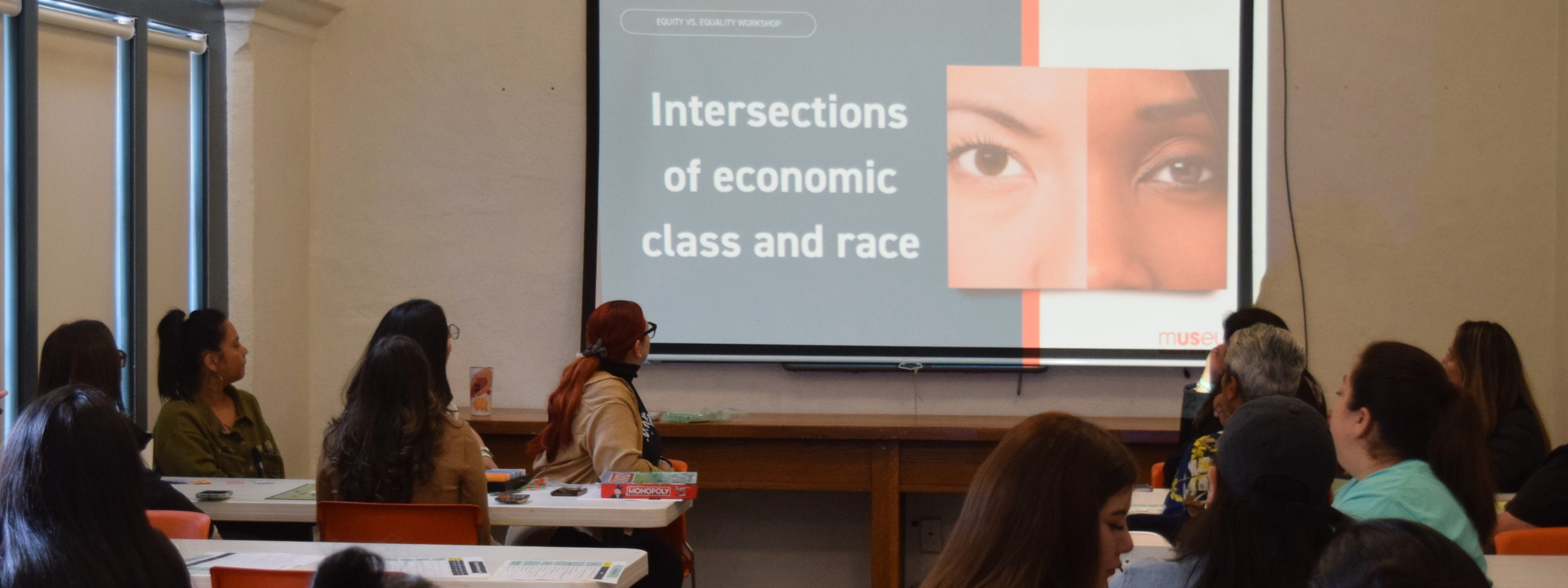 A photo of a group participating in a Race workshop at the Museum. Participants are watching a presentation about the intersections of economic class and race.