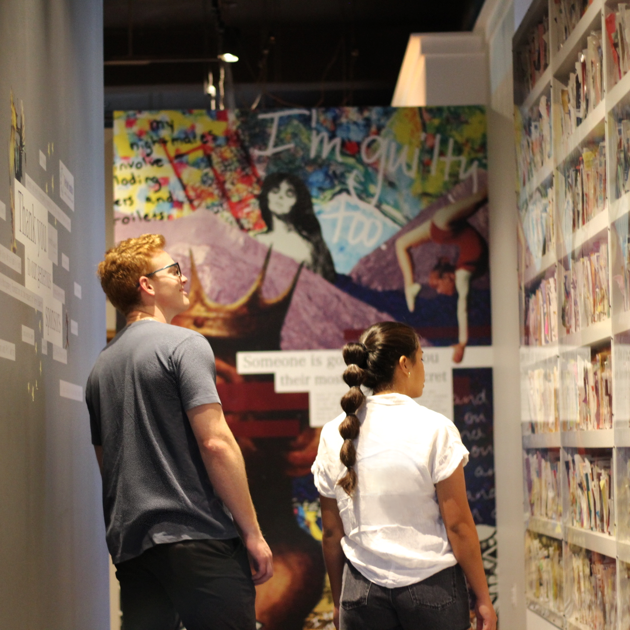 Two people walking down a hallway lined with hundreds of postcards in the "PostSecret" exhibit.