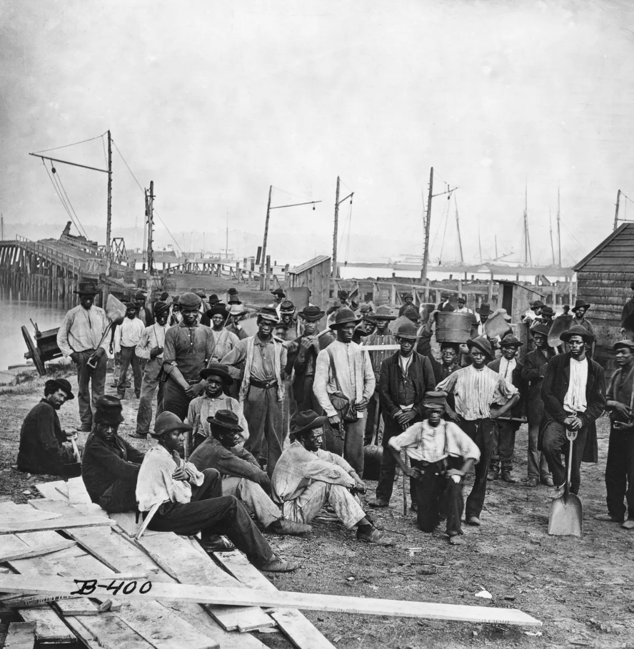 A vintage, black and white photo of a group of individuals in a harbor or shipyard.