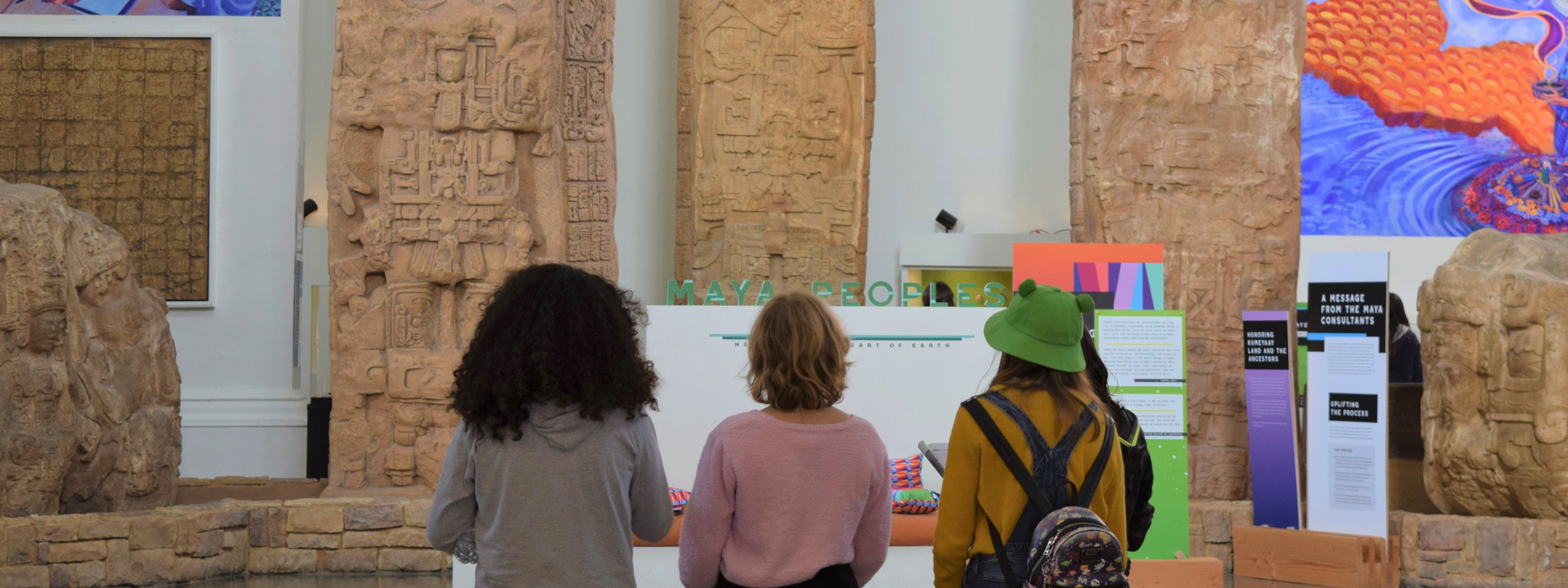 Three young adult visitors walk toward the "Maya Peoples: Heart of Sky, Heart of Earth" exhibit during a group visit to the Museum.